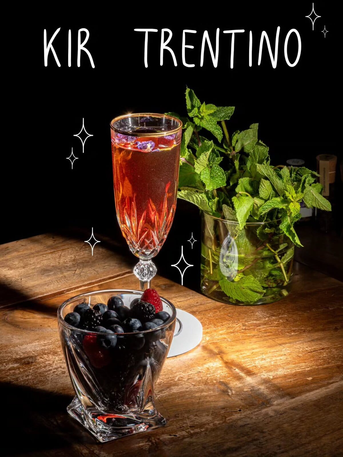 Kir Trentino in un flûte di cristallo, accanto a una ciotola di mirtilli e a un vaso di menta