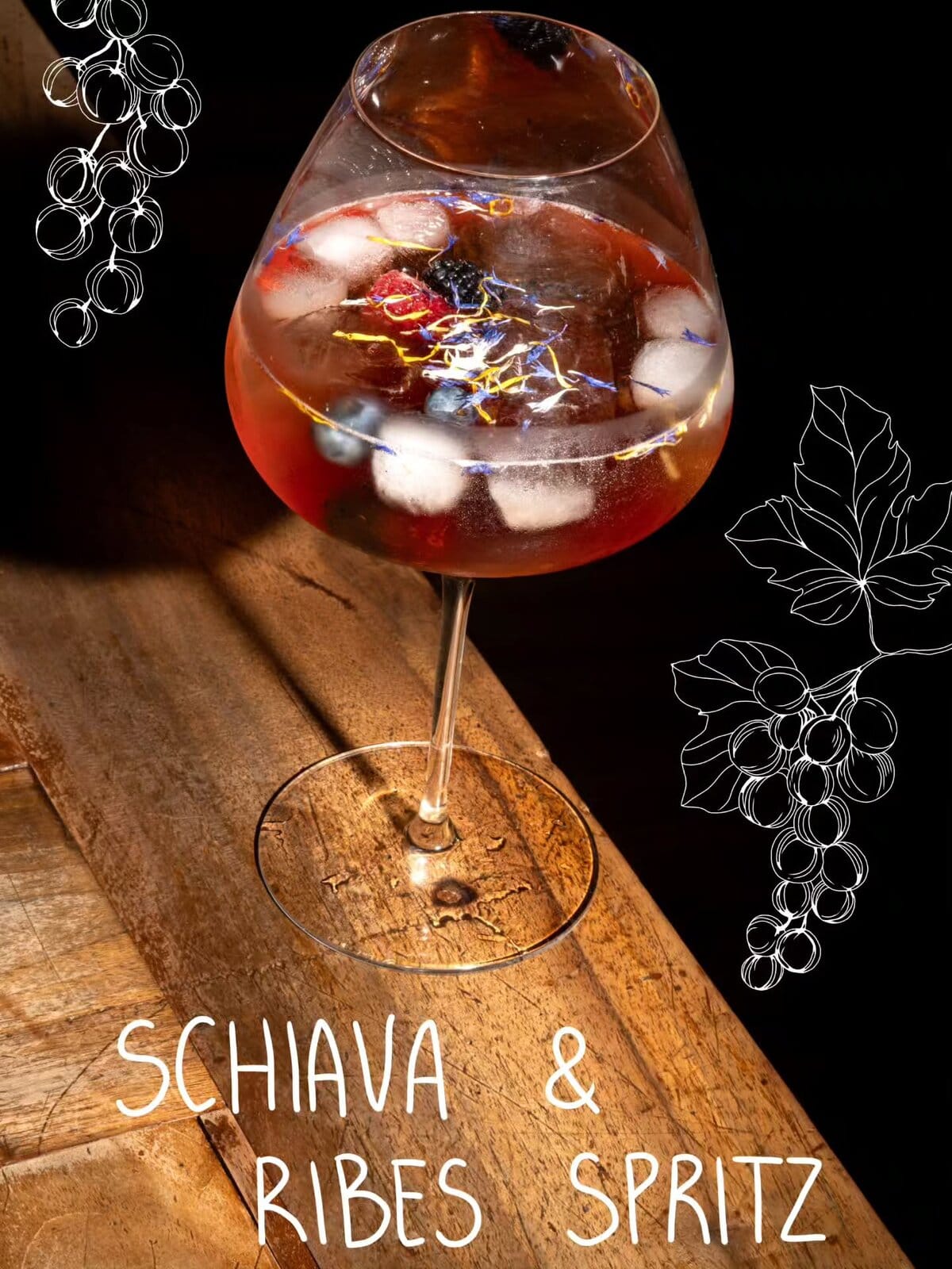 Schiava & Ribes Spritz in un grande calice con ghiaccio e fiori edibili, su un tavolo di legno