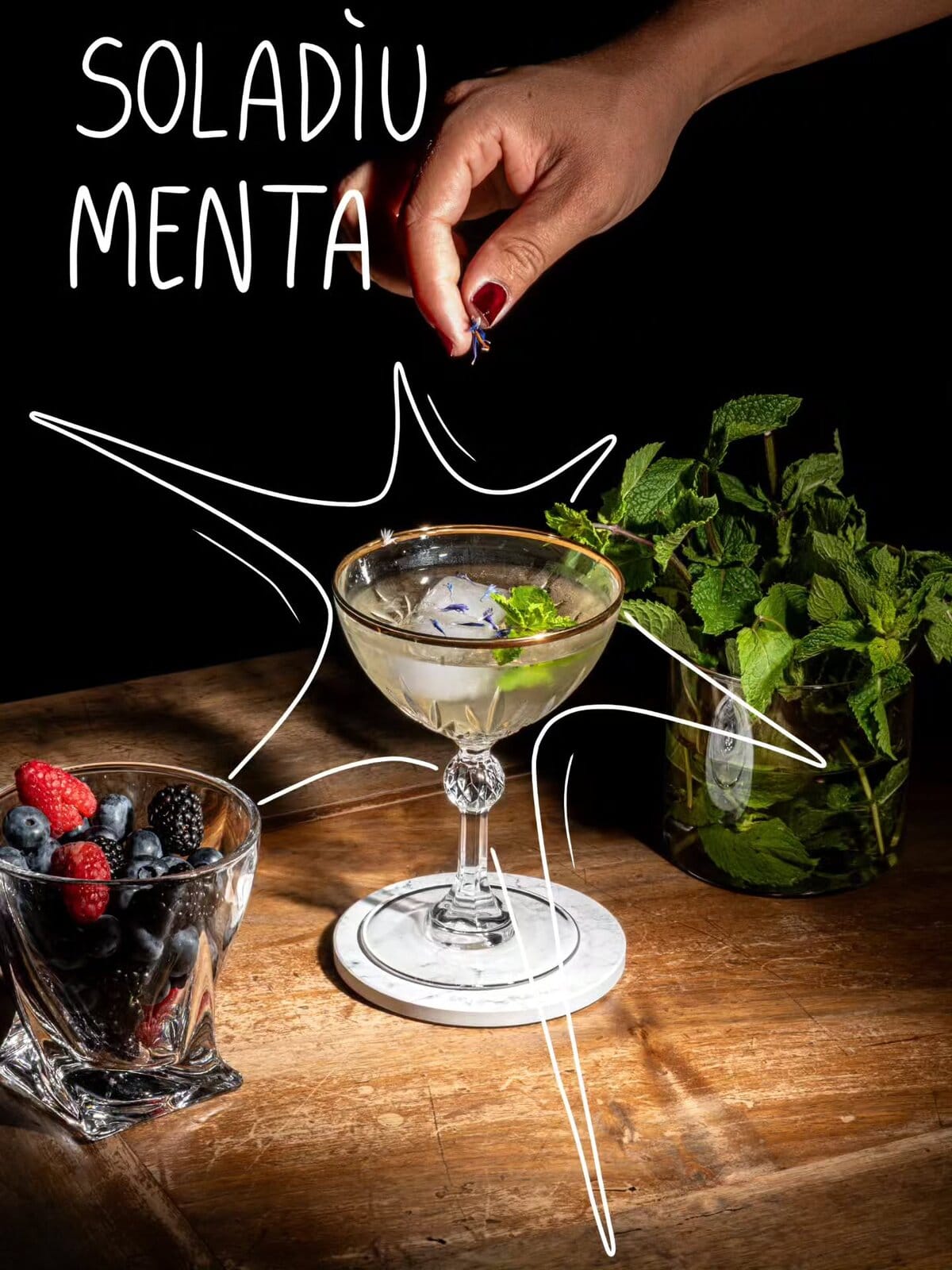 Soladìu Menta servito in una coppa di cristallo con foglie di menta, accanto a una ciotola di frutti di bosco